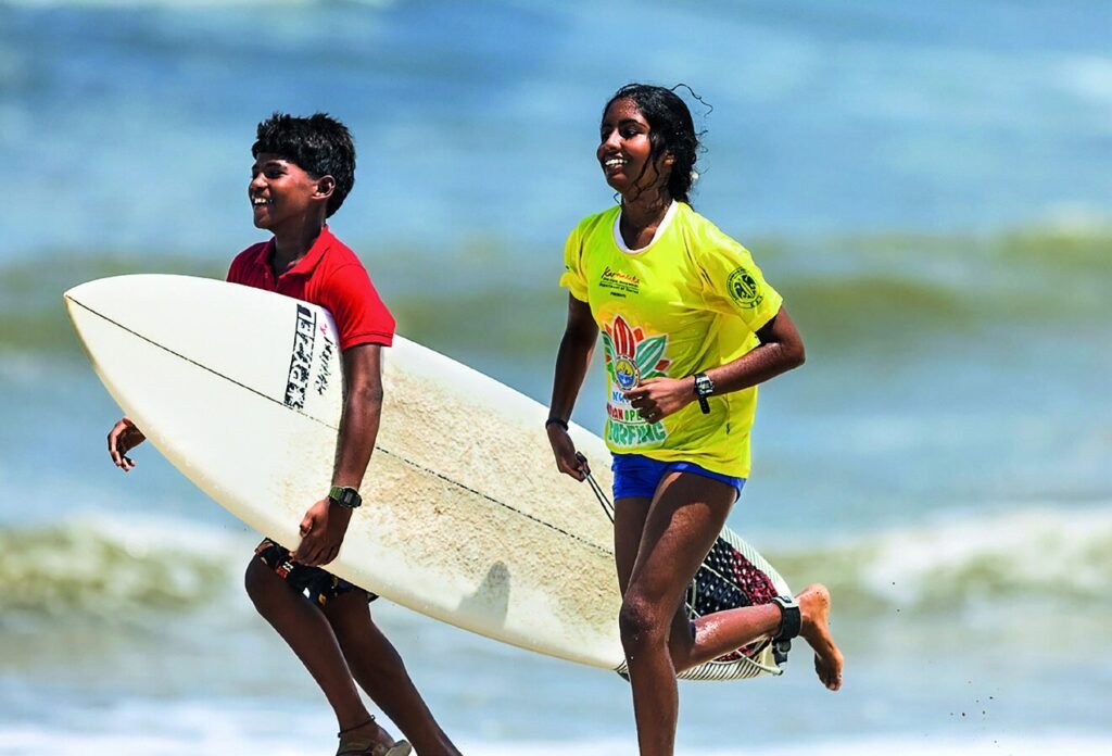 Harish P. and Nethra Arabolu running along Tannirbhavi Beach with a surfboard